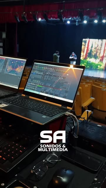 Cabina técnica en sala: consolas de iluminación y sonido con el escenario iluminado al fondo.