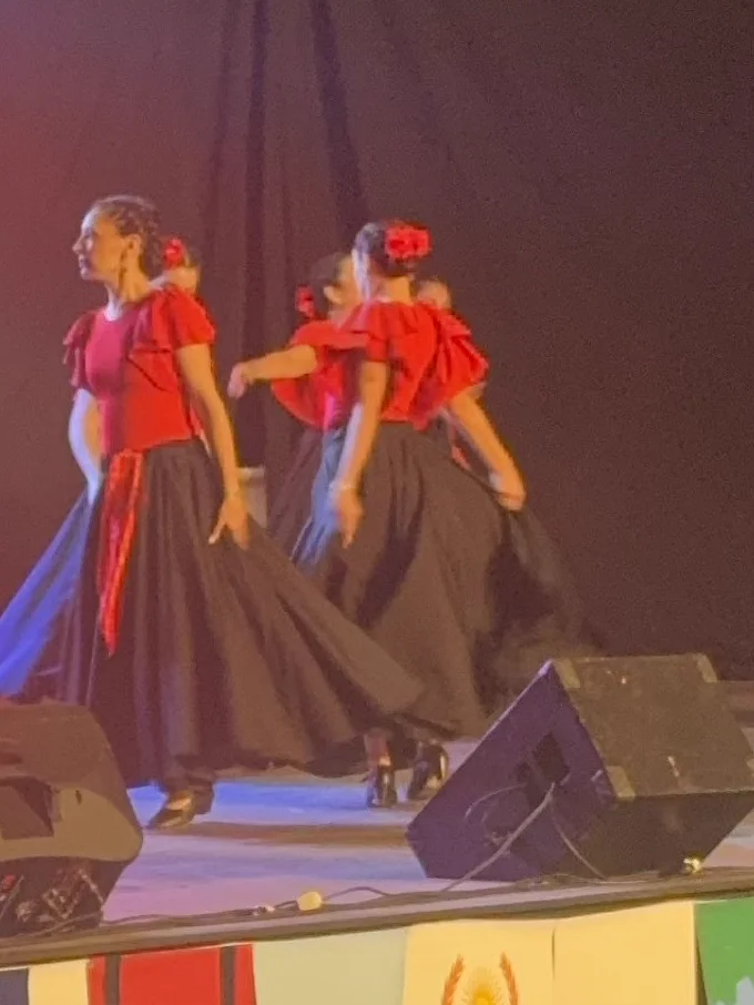 Bailarines vestidos de rojo y negro en movimiento sobre el escenario, con iluminación cálida.